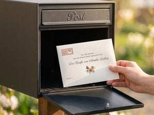 Hand nimmt einen Umschlag der Geschichte "Die Briefe von Amélie Dubois" aus dem Briefkasten